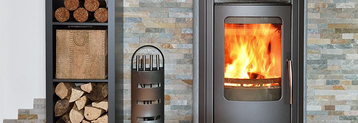 Ein Kaminofen brennt mit Kaminholz im Ständer daneben